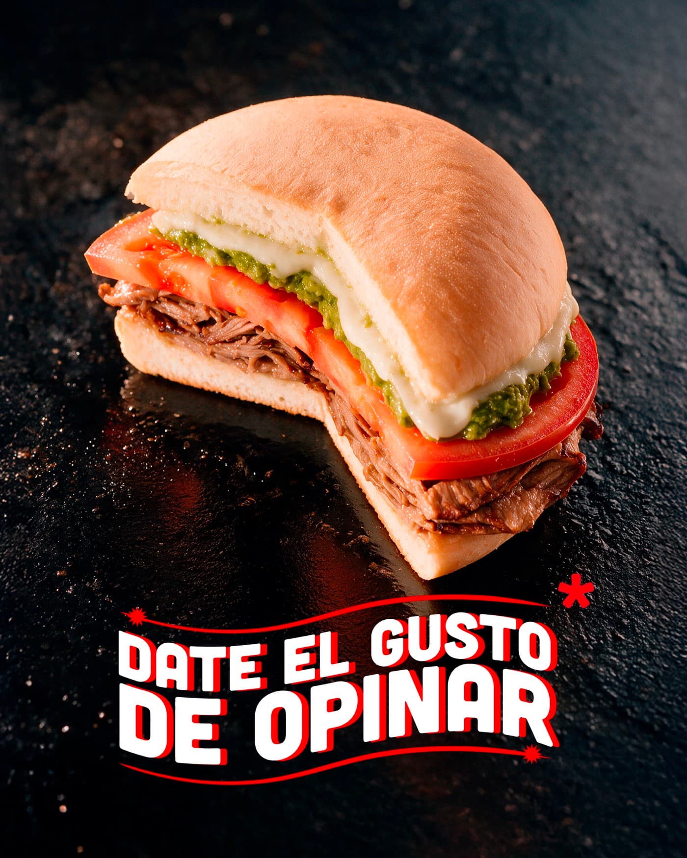 Sándwich de mechada con tomate, palta y queso derretido sobre una superficie oscura